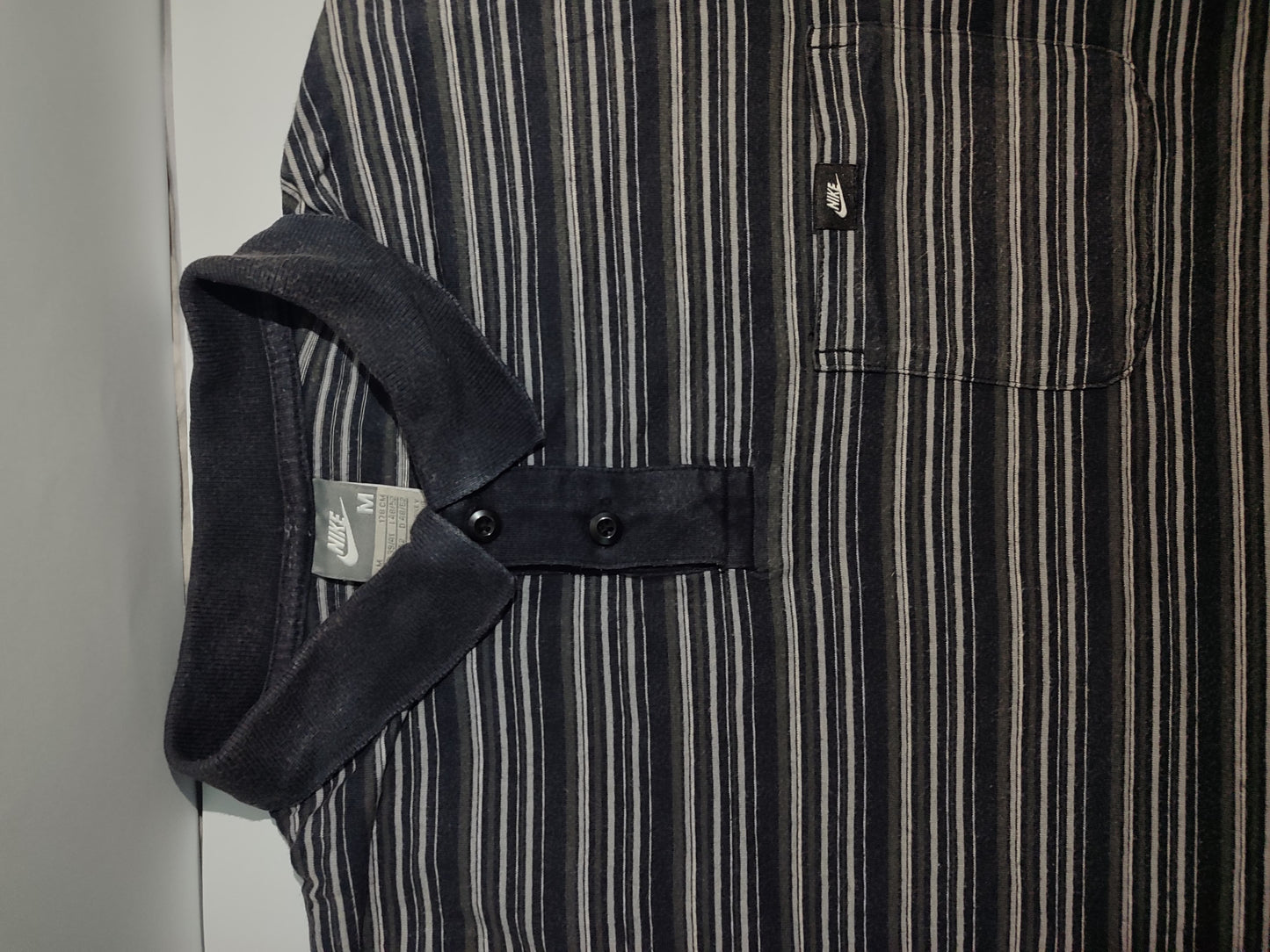 Close-up of a black and white striped shirt with a pocket and strap detail.