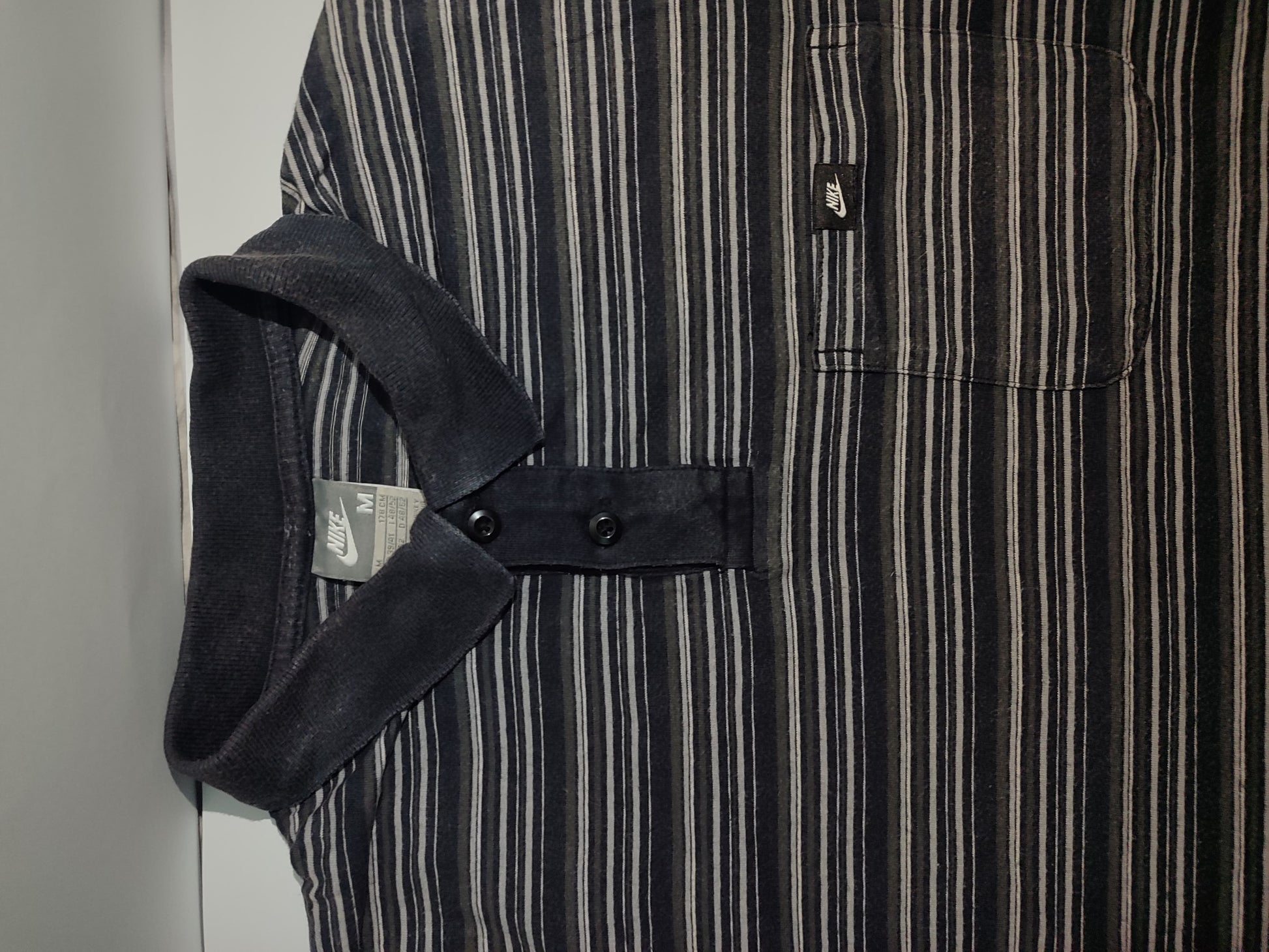 Close-up of a black and white striped shirt with a pocket and strap detail.