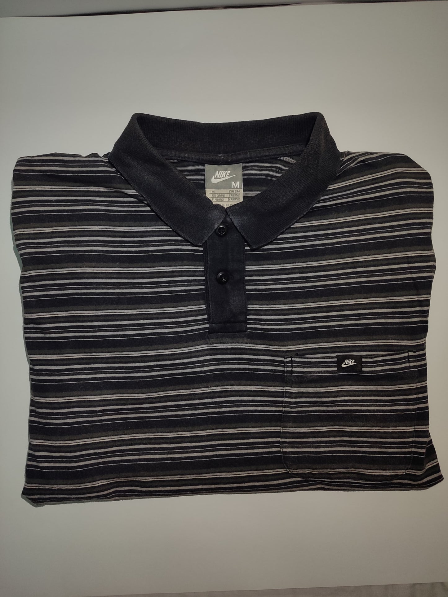 Folded black and gray striped polo shirt with Nike logo on a white background